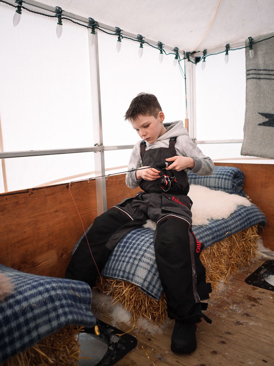 Casual seating area with plaid blankets and hay bales inside a tent.