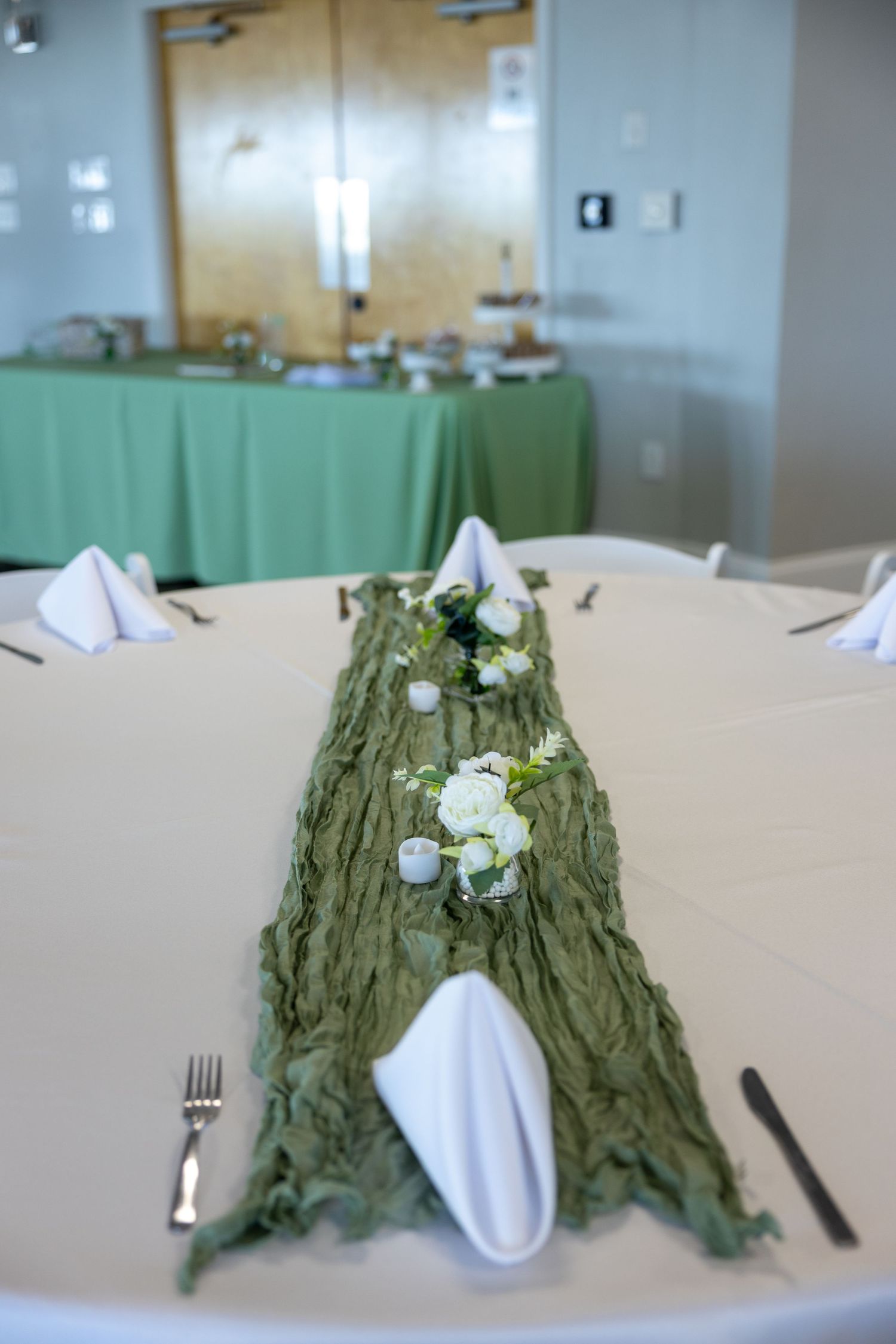 Round banquet table setting with green runner decorated with white flowers and place settings for formal dining event.