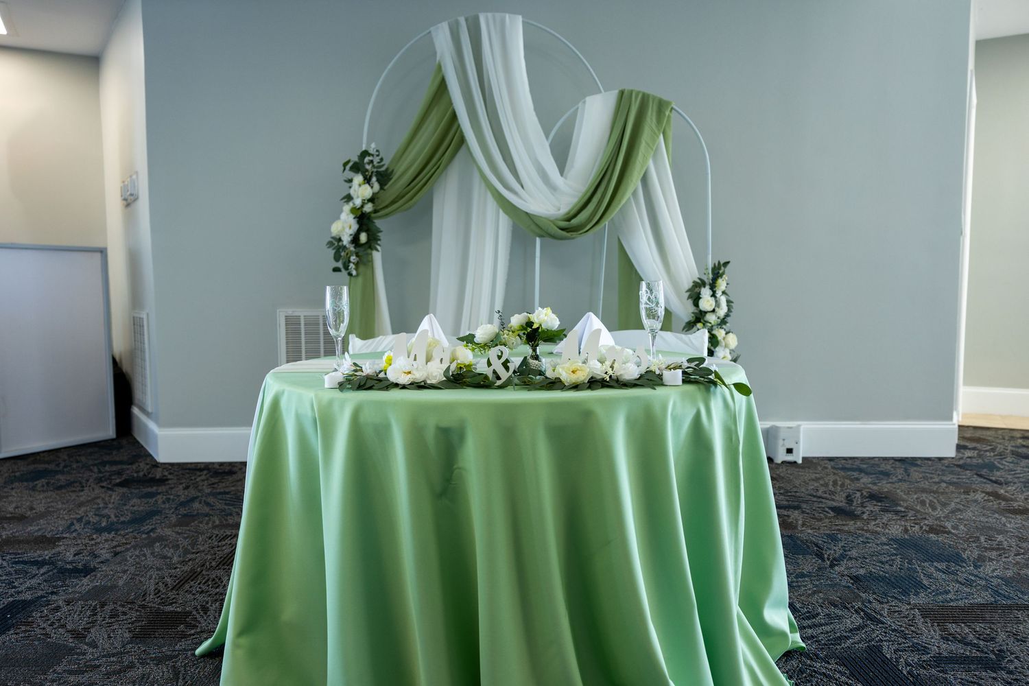 Elegant sweetheart table with mint green tablecloth and white fabric draping decorated with floral arrangements.