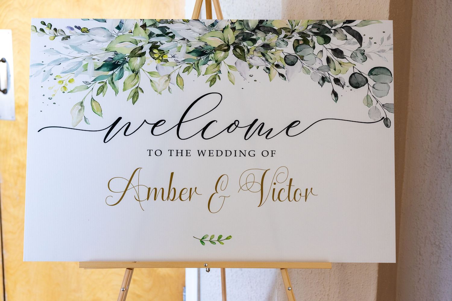 Elegant wedding welcome sign with watercolor greenery and calligraphy text against white background.