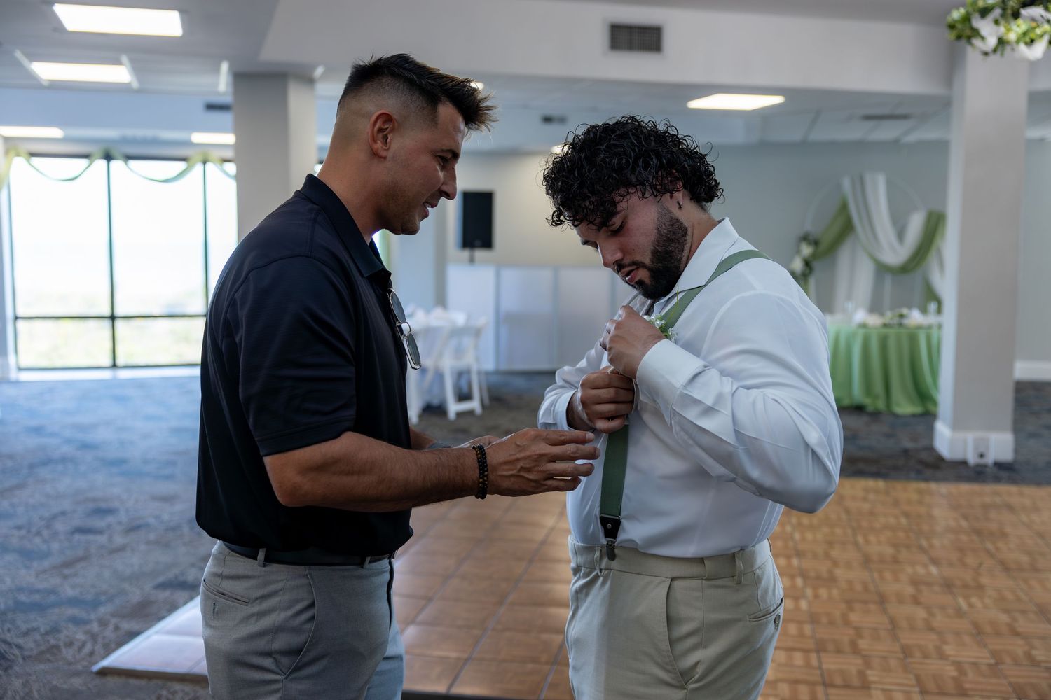 Two men in business casual attire interact in an open office space with carpeted floors and fluorescent lighting.