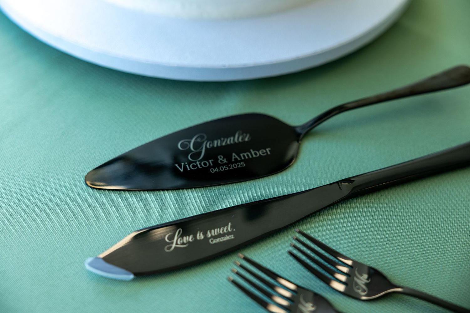 Black serving utensils with elegant script text displayed on a mint green table setting with white plates.