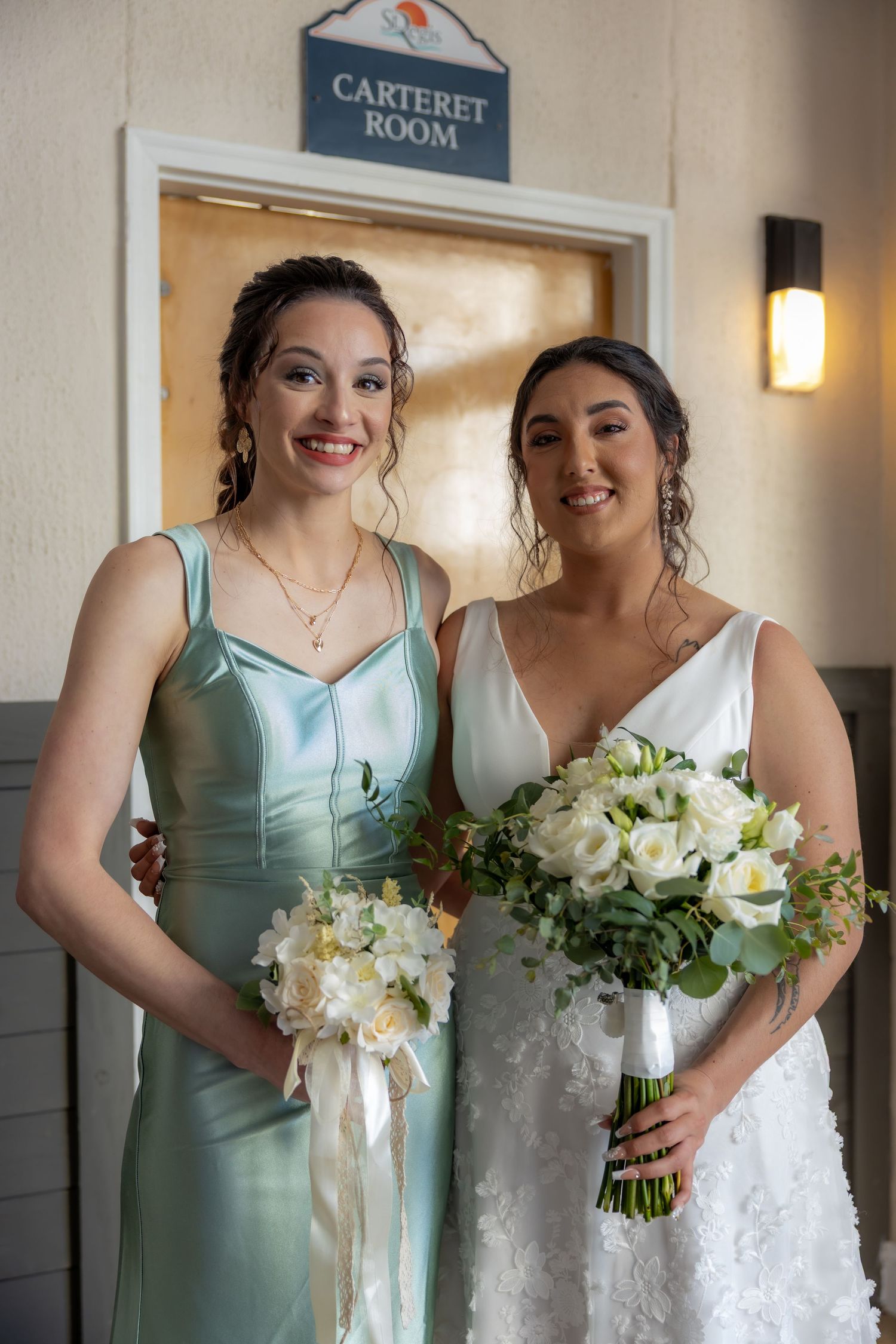 A wedding photo showing the bride in white with her bridesmaid in a mint green dress, both holding beautiful bouquets.