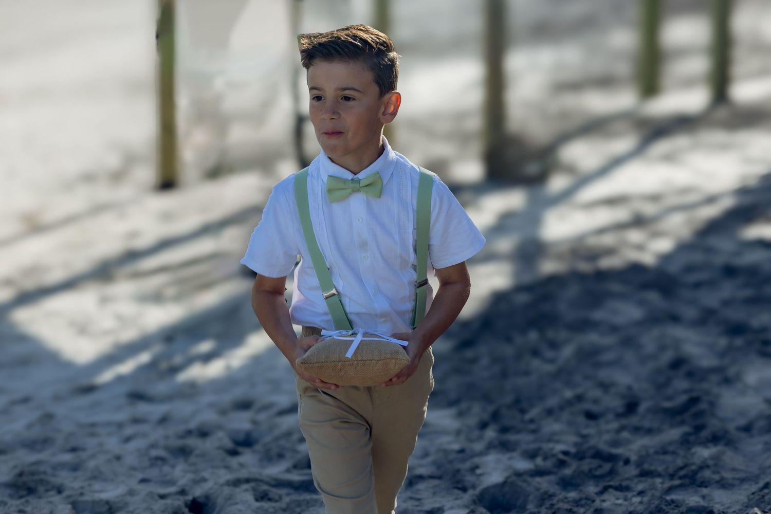 A child in a white polo shirt and khaki pants stands confidently on a sandy path in bright sunlight.
