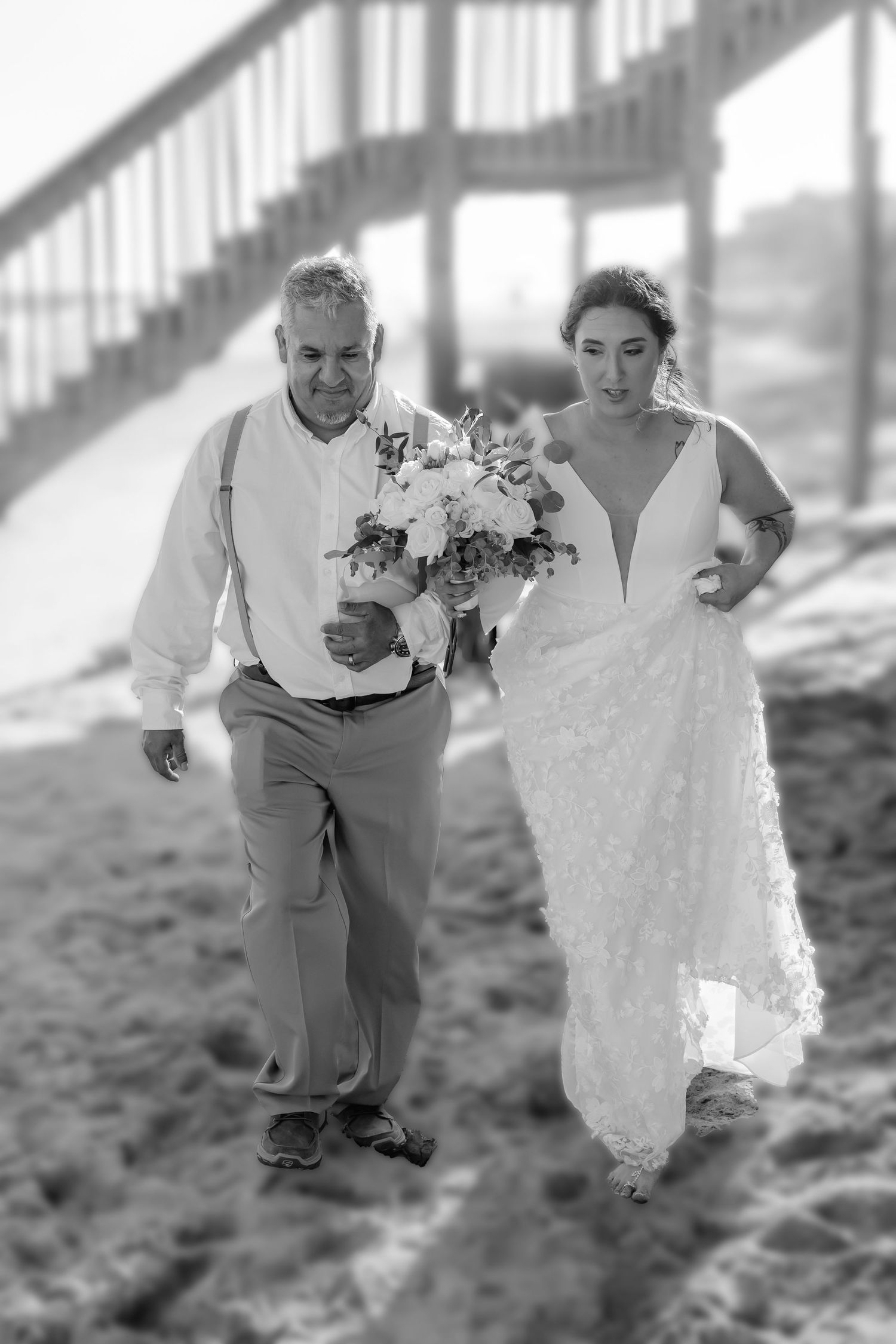 Black and white beach wedding photograph showing a couple walking together on sand with a beautiful floral bouquet.