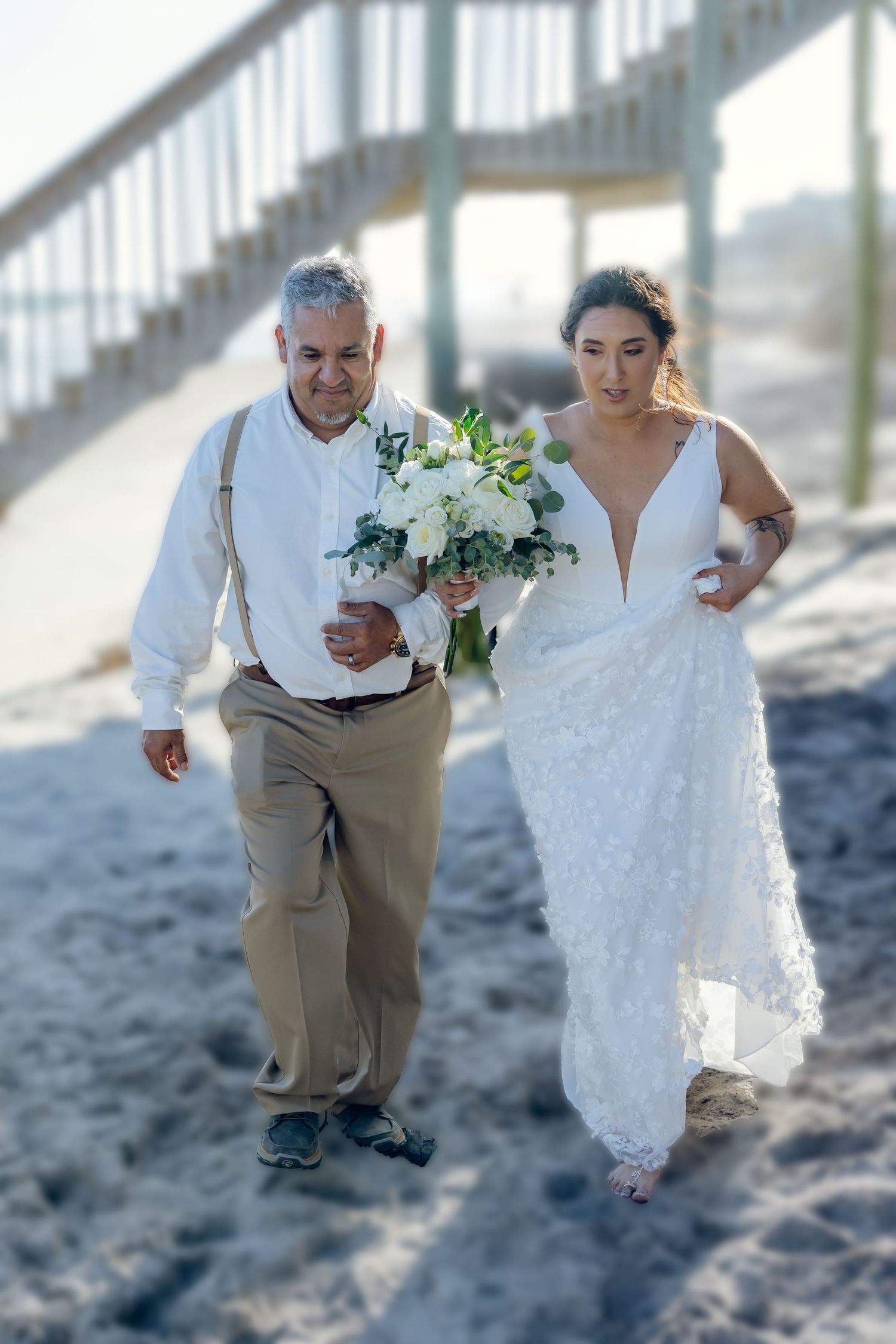 A couple walks arm in arm on a beach during a wedding ceremony, with the bride wearing a white lace gown.