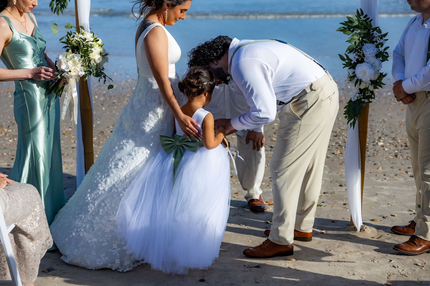 People celebrating a beach wedding ceremony with white dress and khaki pants on a sunny tropical shore.