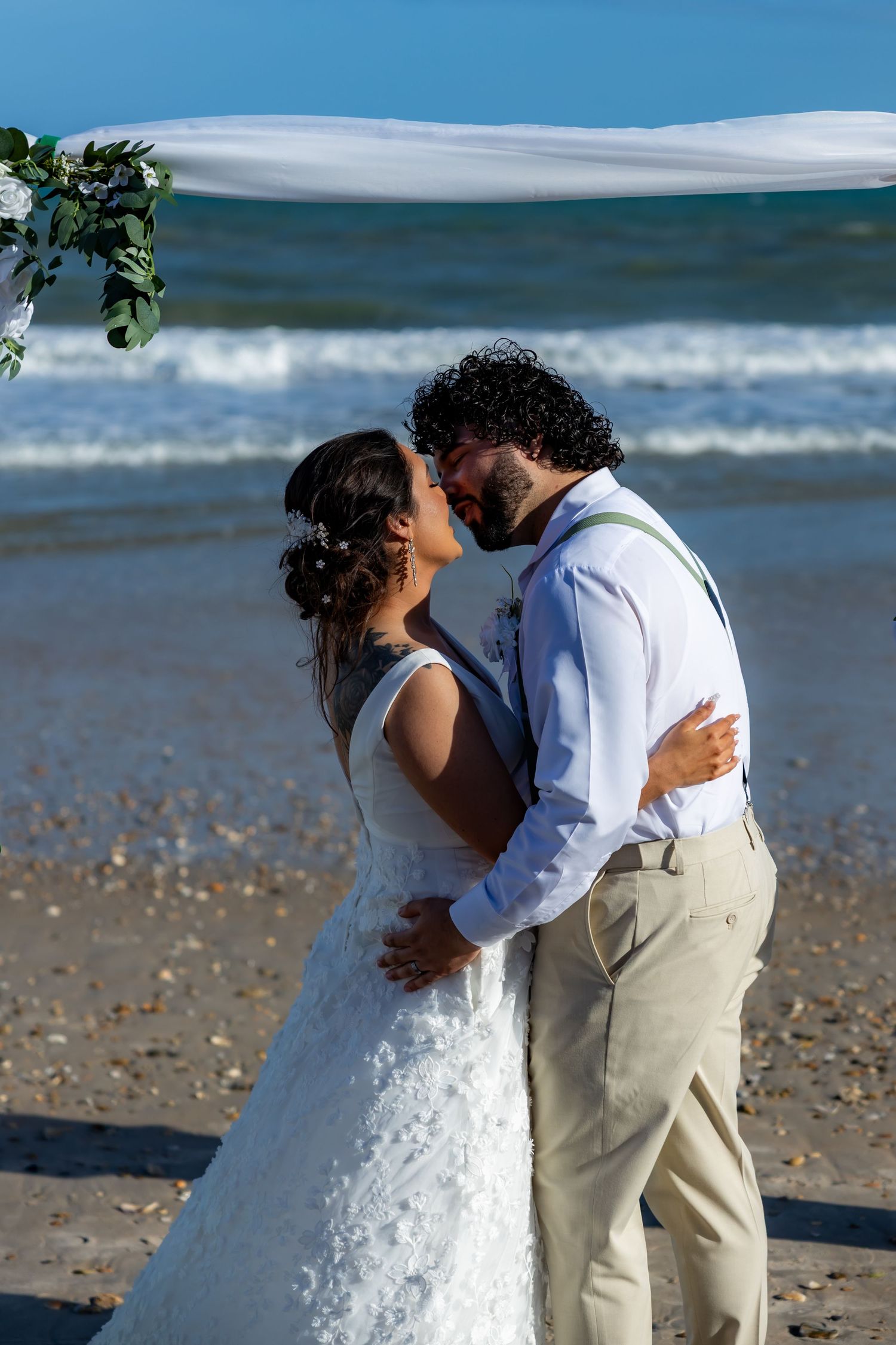 Couple embracing on sandy beach with ocean waves and blue sky in background.