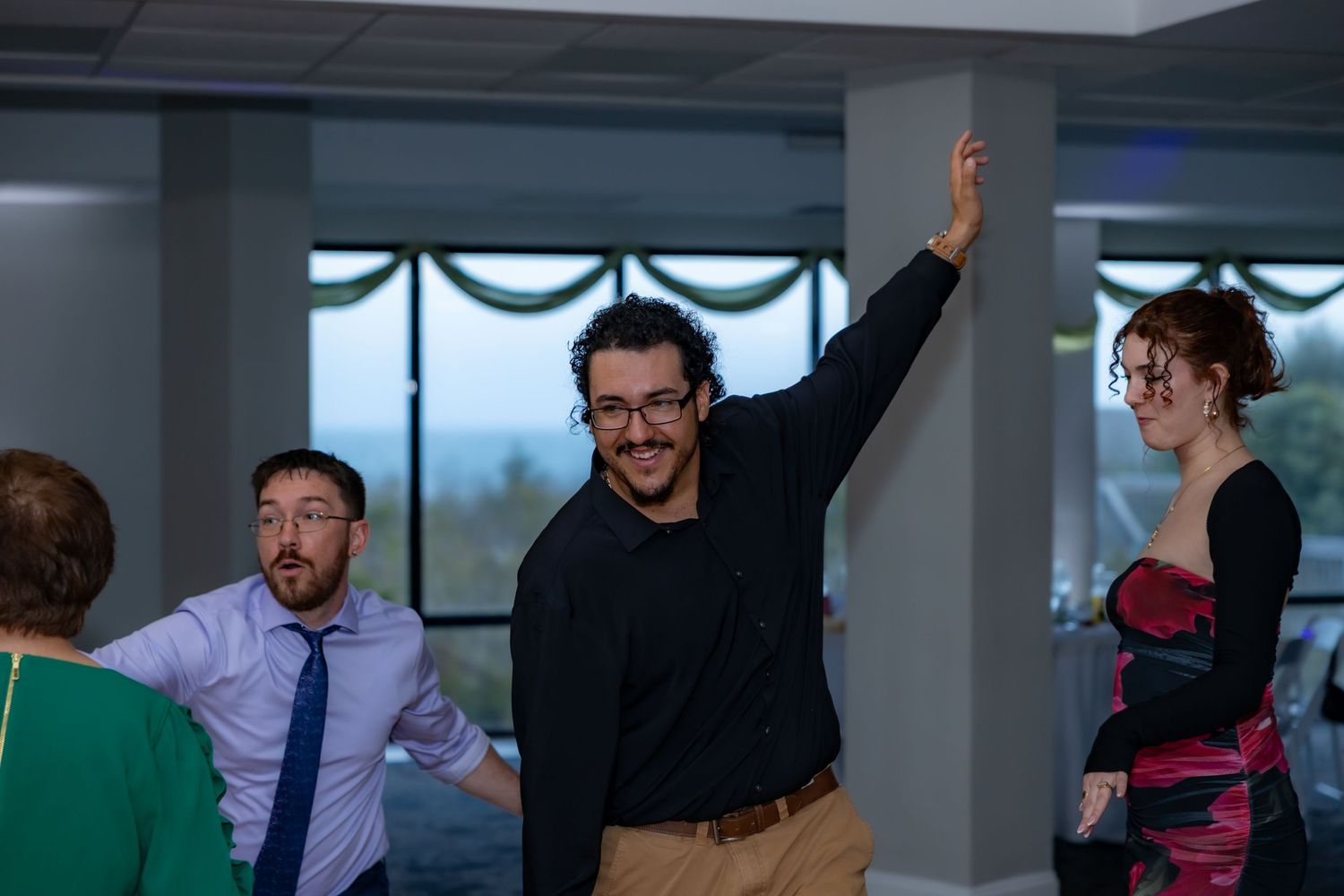 Wedding guests dance and celebrate with raised arms during a reception in a decorated venue.