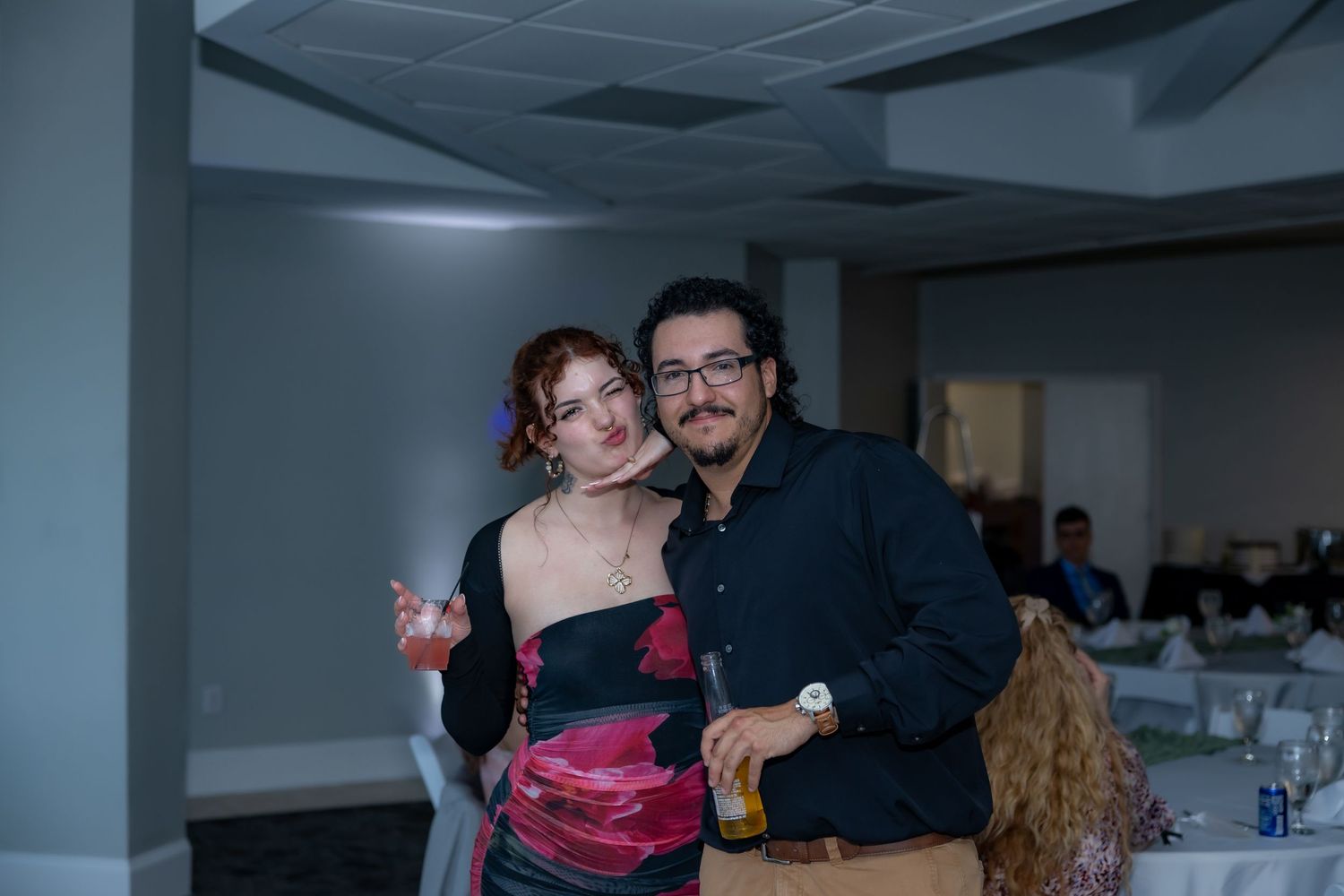 Two people in formal attire dance together at an indoor event with a pink dress and black shirt visible.