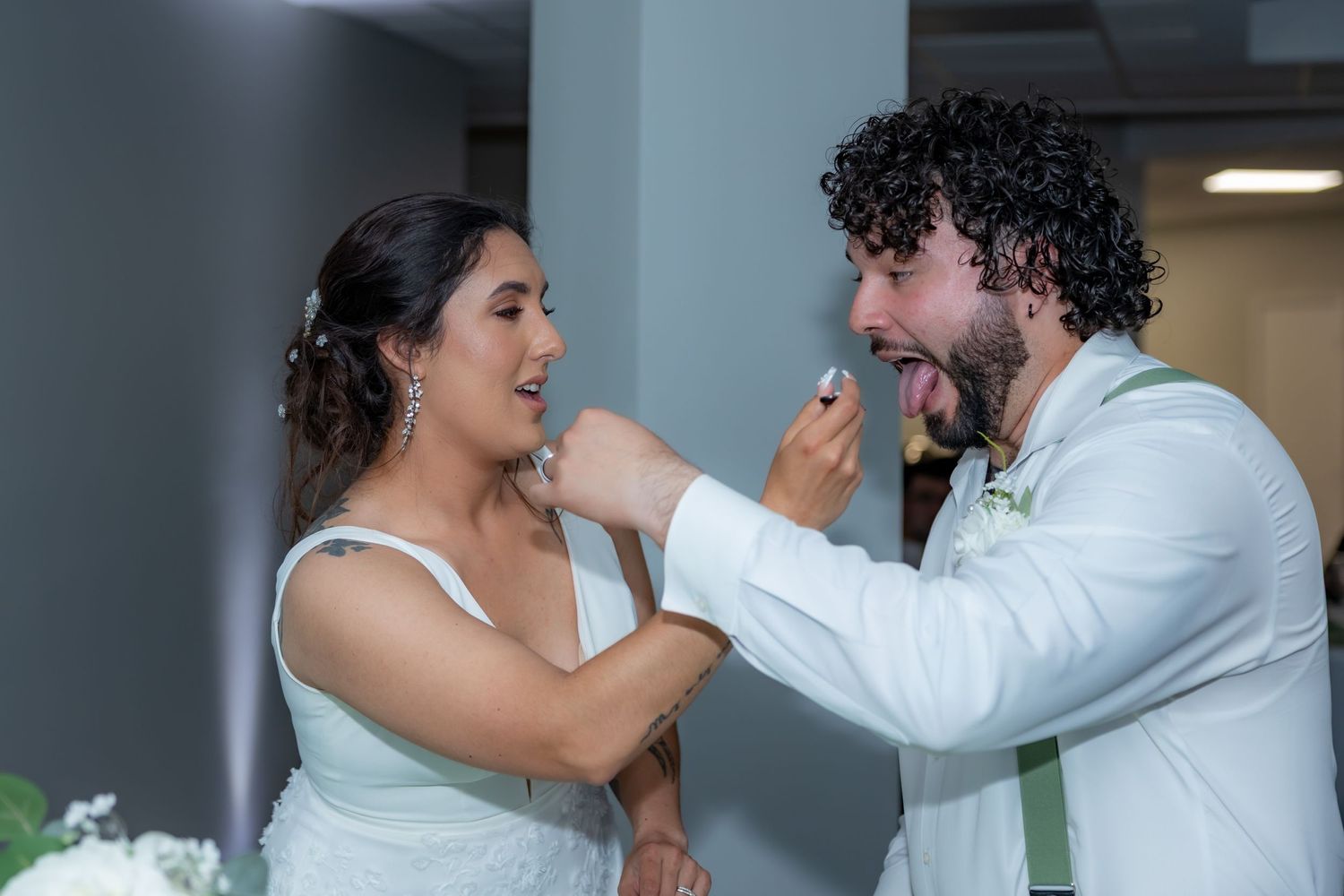 A newlywed couple playfully feeds each other cake during their wedding reception.
