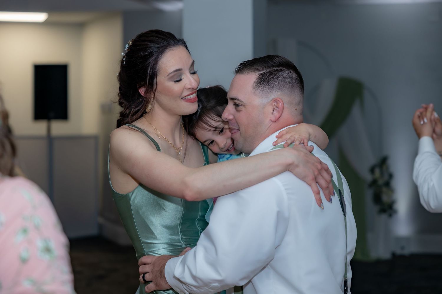 A couple dances closely together at a party, with the person in a sage green dress embracing their dance partner in white.