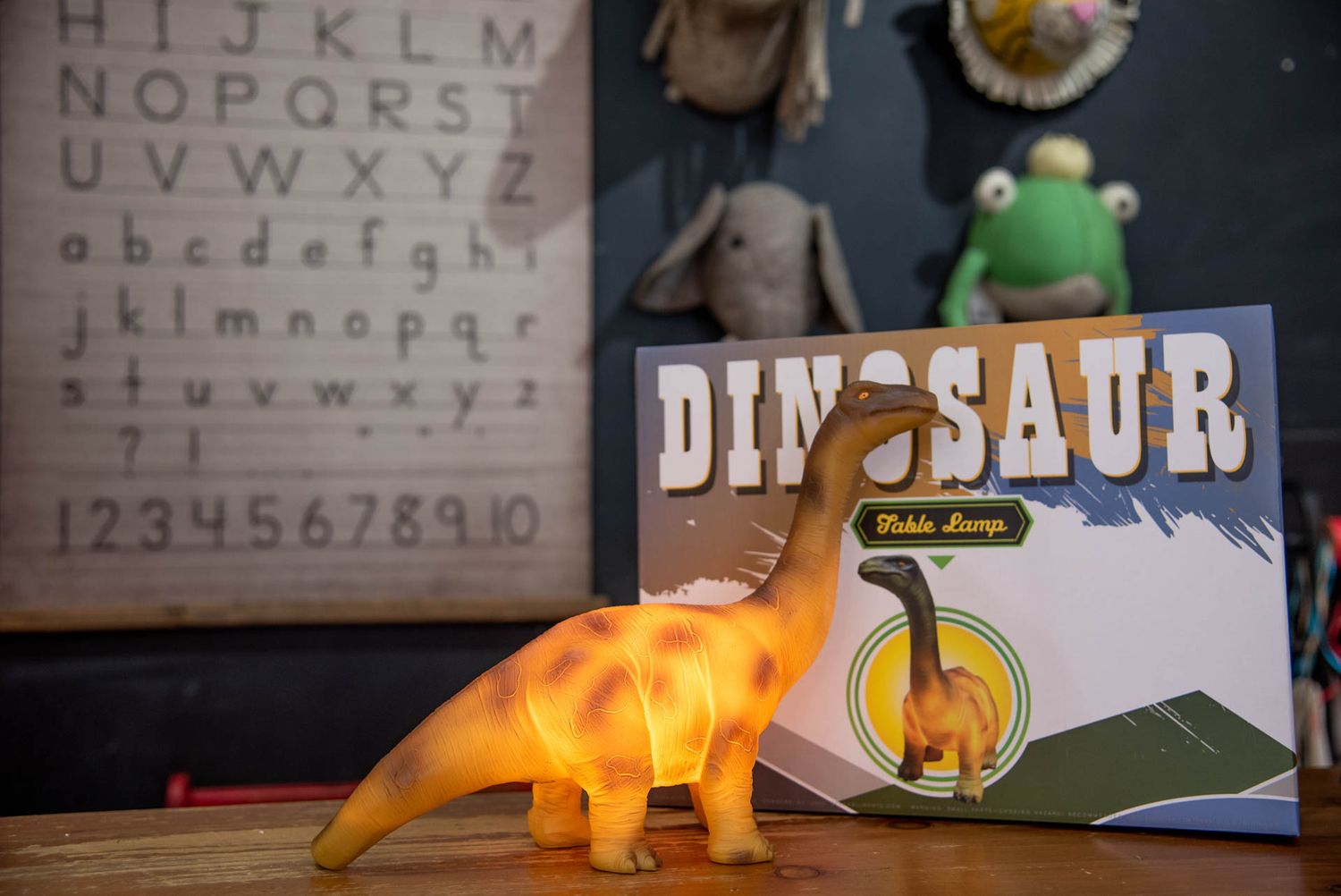 A glowing orange dinosaur toy sits beside a book titled 'Dinosaur' with an eye chart and plush toys in the background.