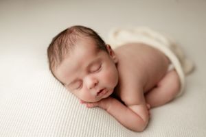 Sleeping newborn baby lying on soft white fabric in peaceful pose during professional portrait session.