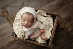 Newborn baby sleeping peacefully in wooden crate lined with vintage lace and white wrap during professional photo session.