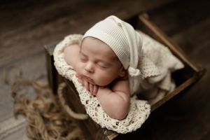 Peaceful sleeping newborn wrapped in delicate lace blanket rests in rustic wooden box.