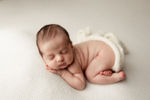 Peaceful newborn baby sleeping on white textured surface wearing cream diaper cover.