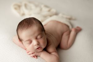 Peaceful sleeping newborn baby lying on soft cream textured backdrop during professional photography session.
