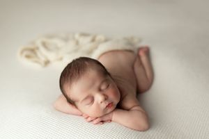 Peaceful sleeping newborn rests on soft white fabric with serene expression and folded arms.