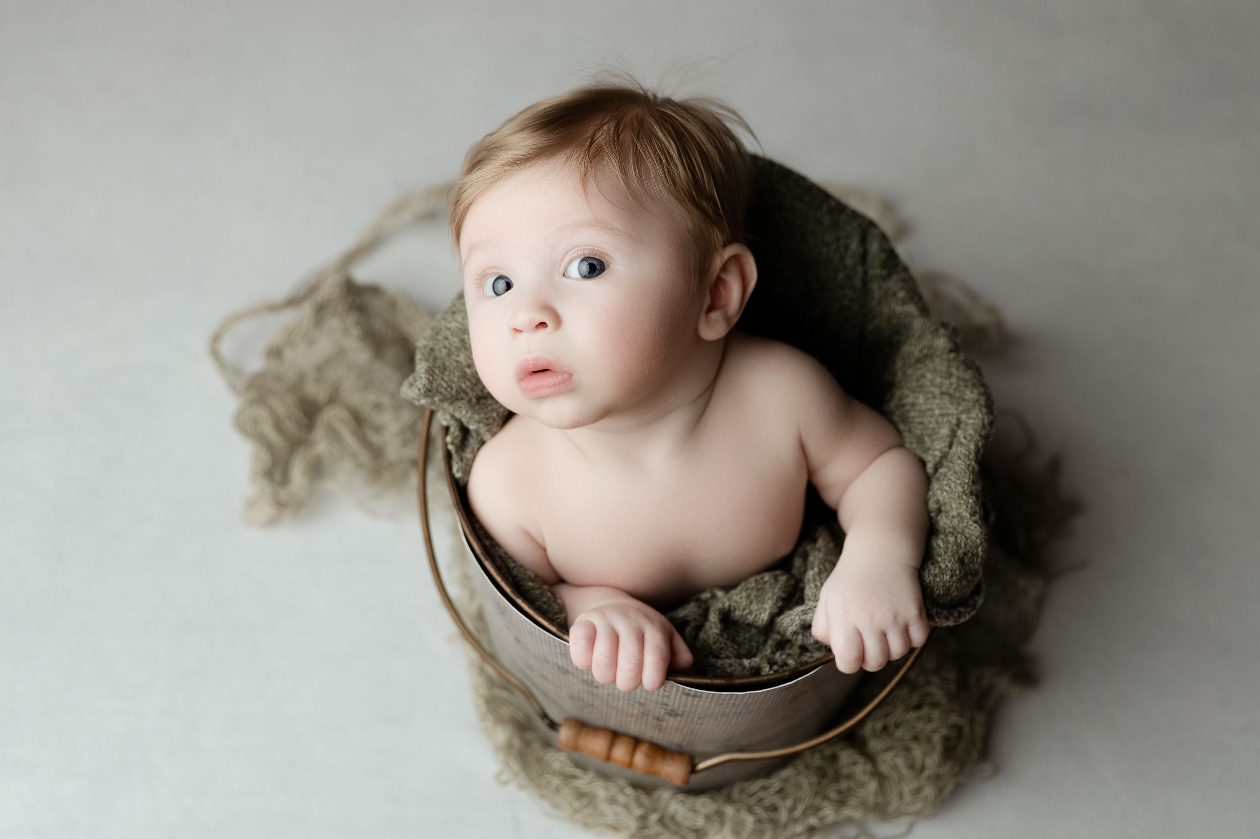 Baby wrapped in soft beige fabric lying in a wooden bowl against light background in artistic portrait.