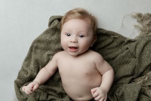 Happy baby resting on olive green blanket during minimalist photography session.