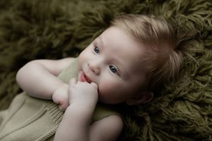 A small child lying on a green blanket with a finger in their mouth.
