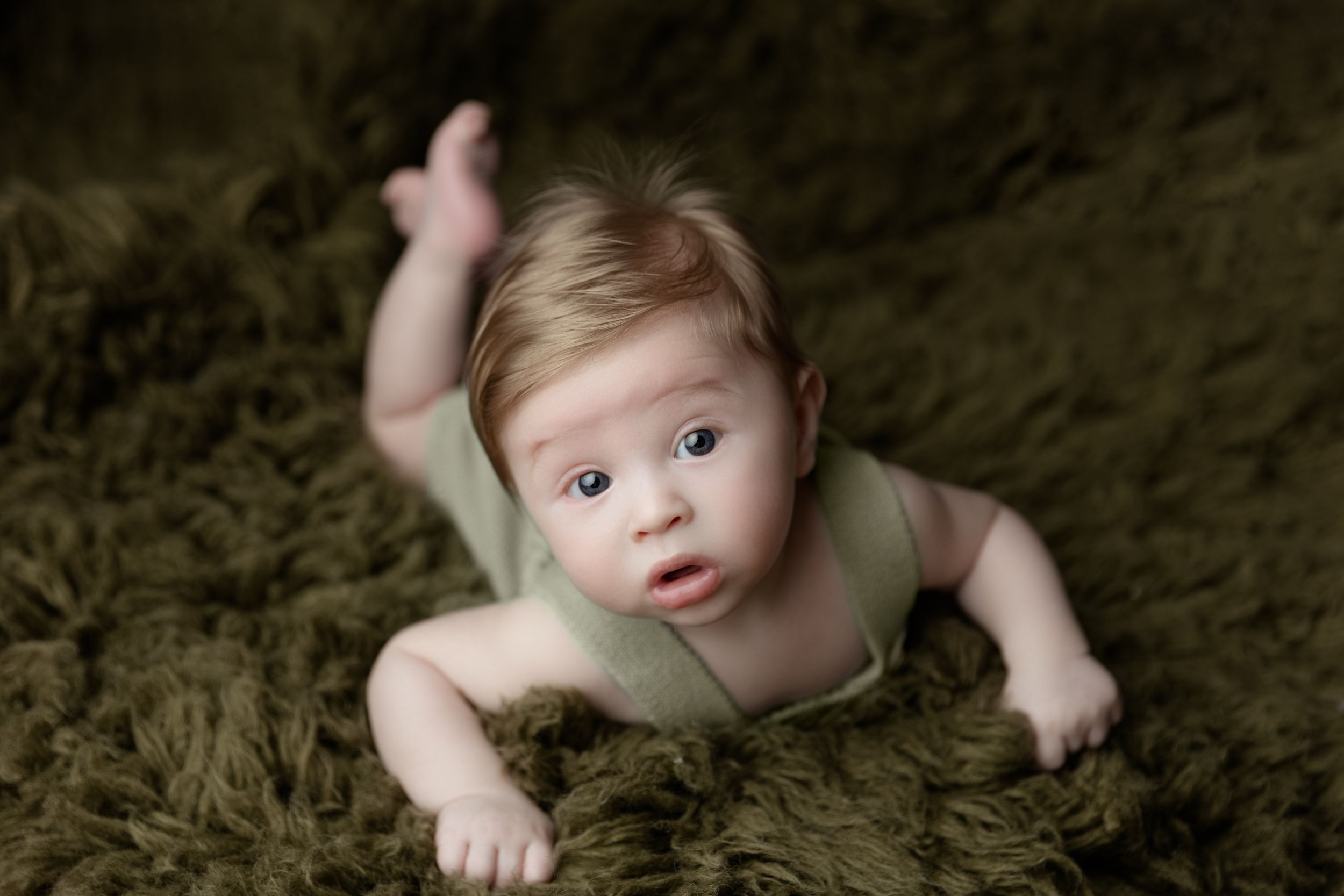 Baby laying on soft olive green textured blanket in professional studio portrait setting.