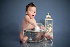 A baby sits in a glass bowl during a studio photo session with a glowing lantern decoration.