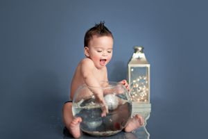 Baby sitting in metal basin next to decorative lantern against blue background during photo session.