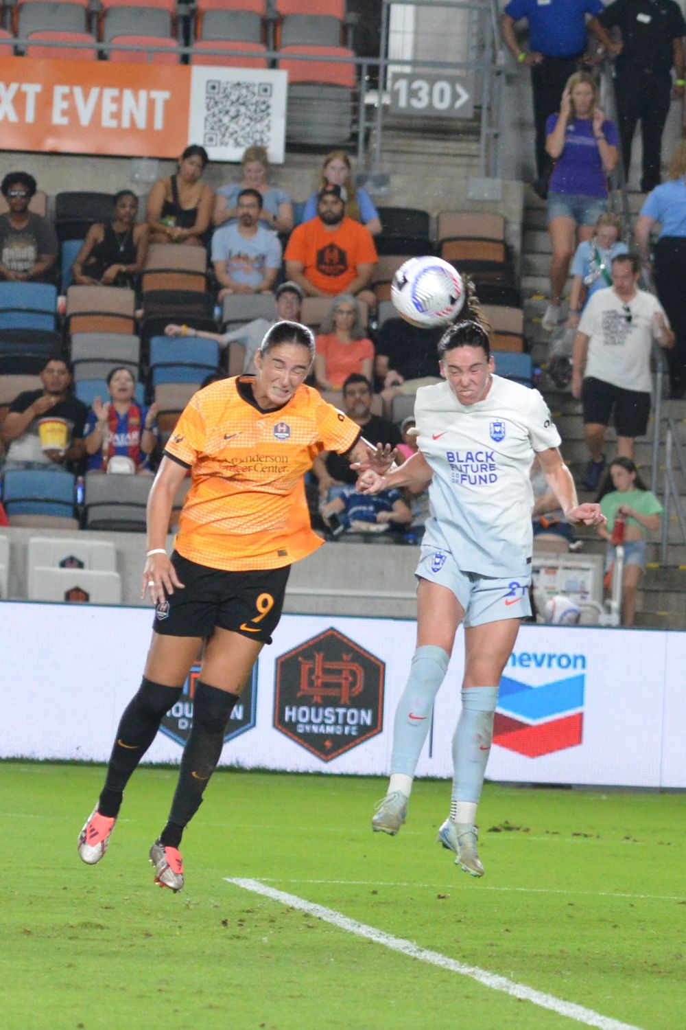 Players from opposing teams leap to head the ball during aerial challenge.