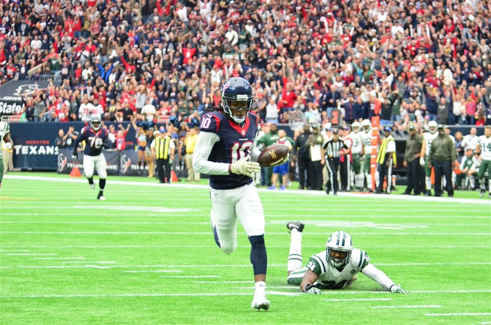 NFL player runs with football while opponent falls on field during game.