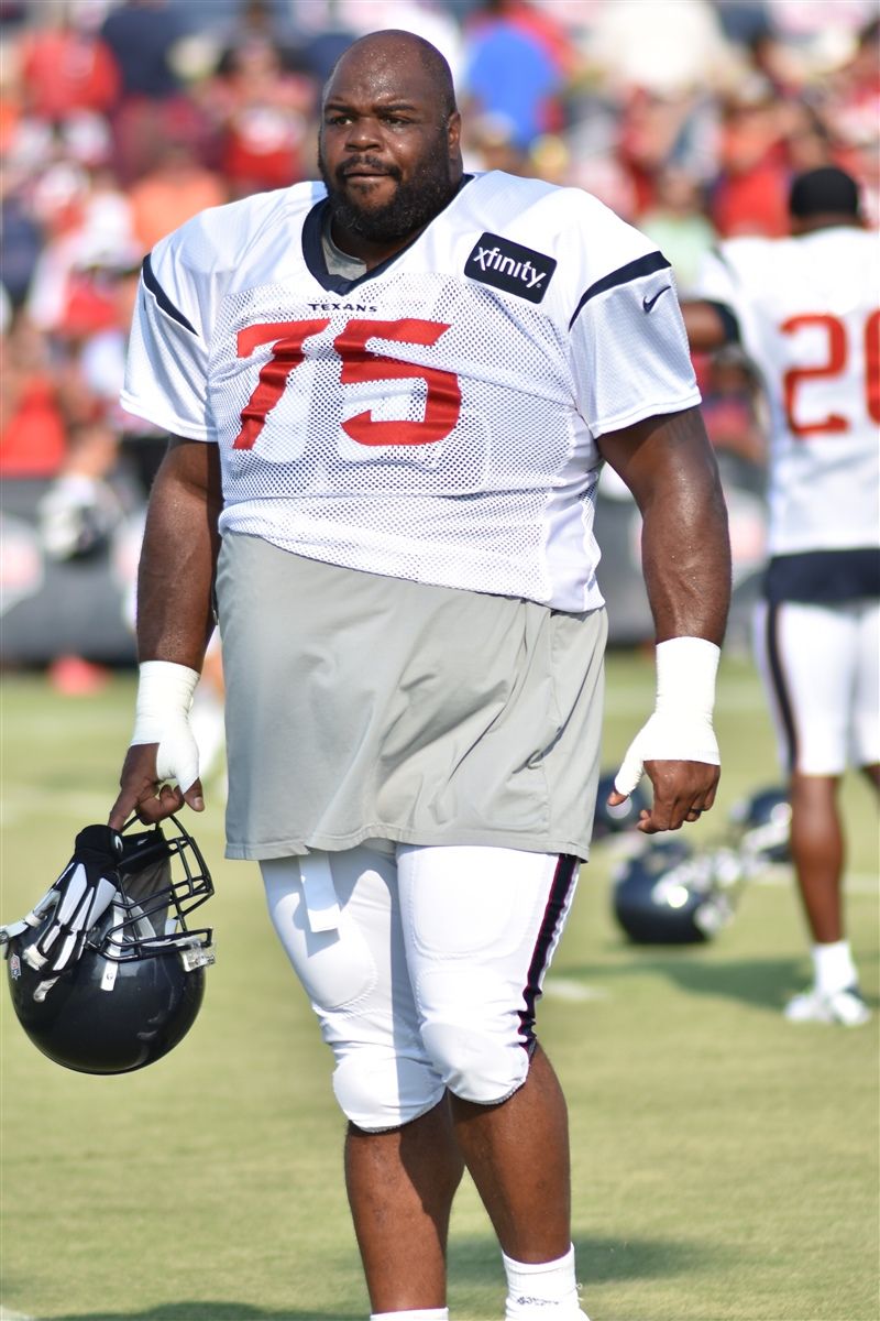 NFL player in white practice jersey holds helmet during training camp.