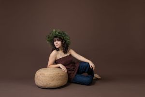 Artistic portrait with leafy crown and brown dress against dark background.