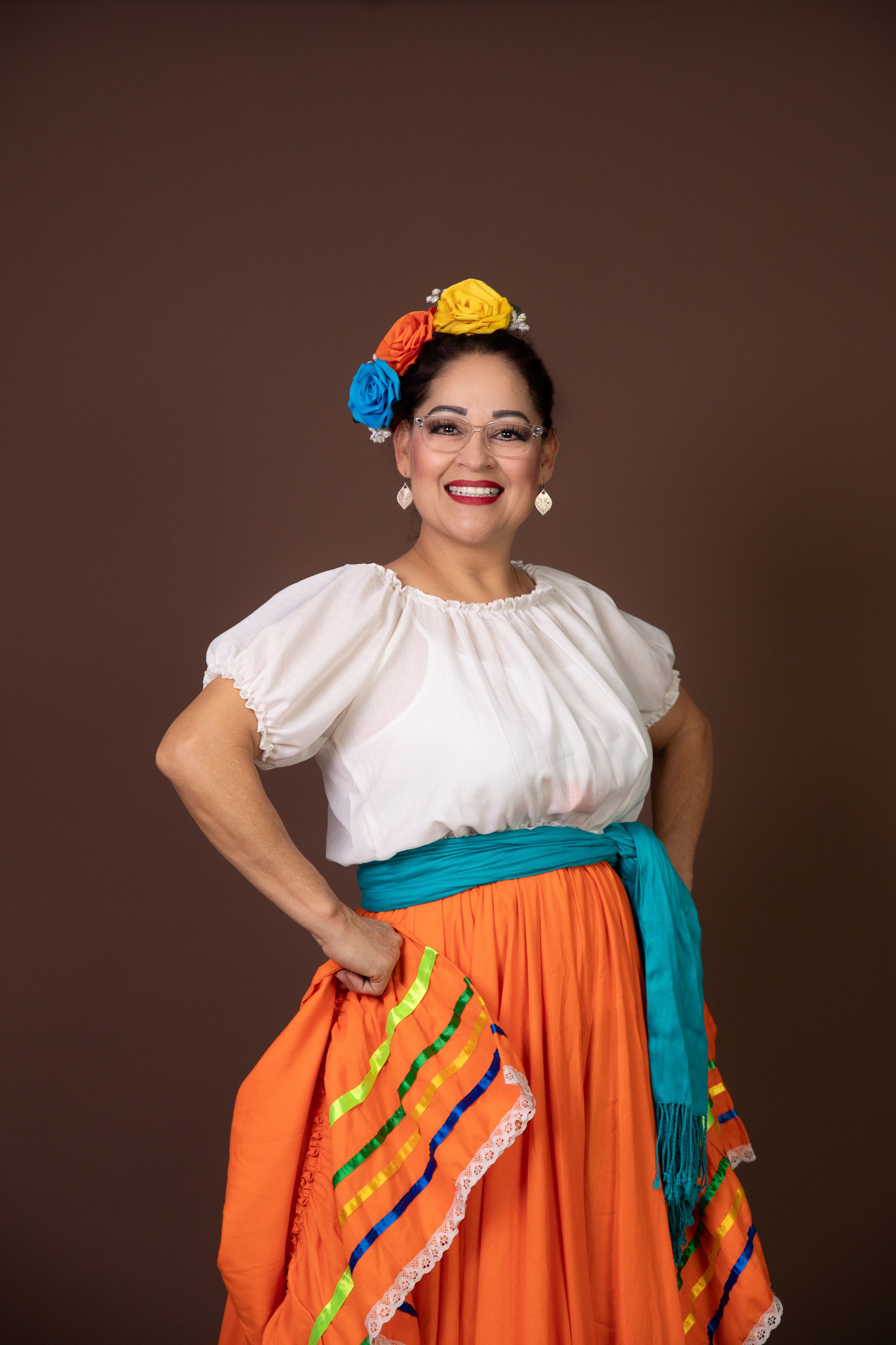 Dancer wearing traditional Mexican costume with orange skirt and colorful accessories.