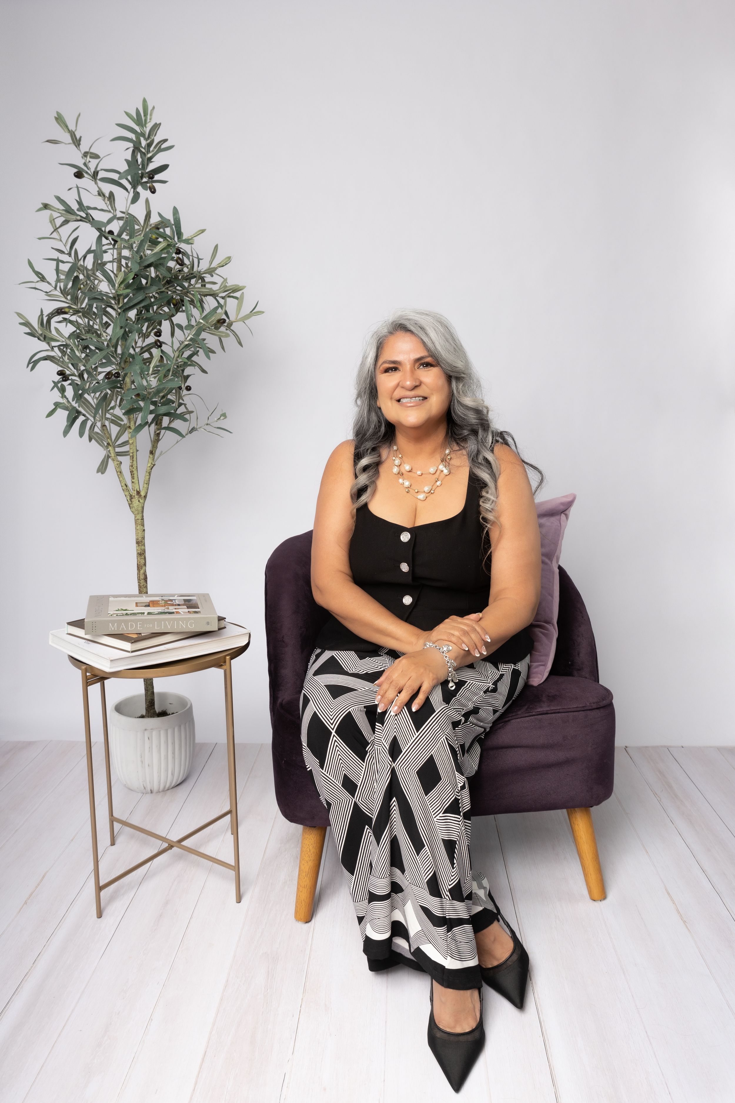A modern lifestyle portrait in a minimalist setting with a houseplant on a gold accent table and purple armchair.