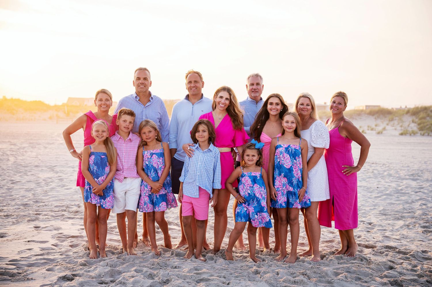A large group poses together on a beach at sunset wearing coordinated bright blue and pink summer outfits.