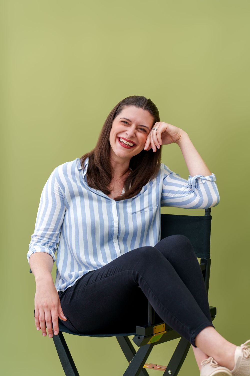 Person in striped blue and white shirt sitting casually in director's chair against olive green background.
