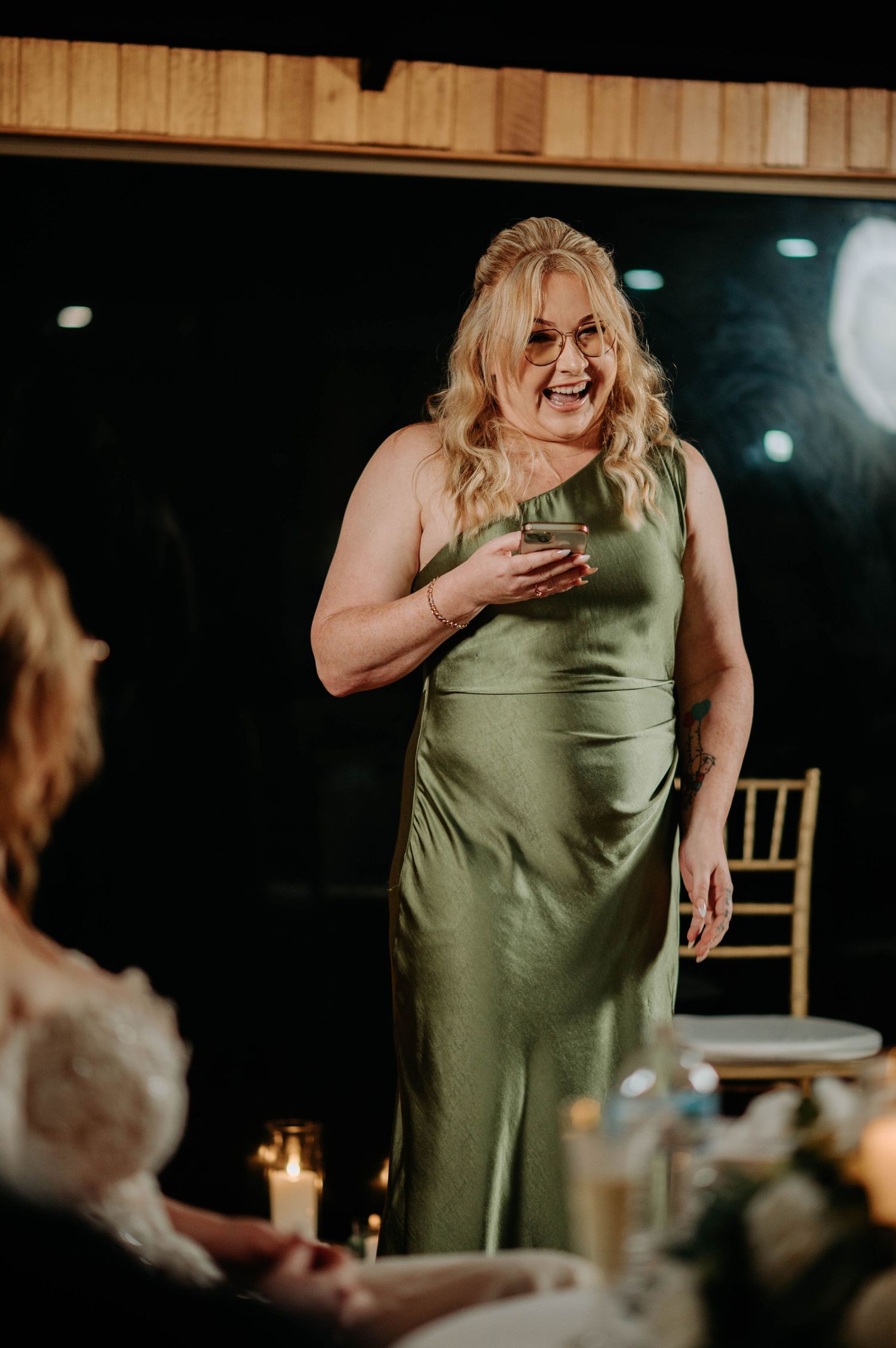 Woman in sage green formal dress laughing during wedding celebration.