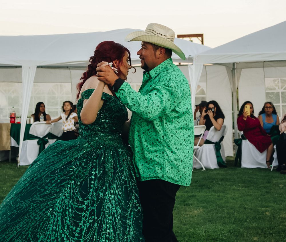 Couple dancing at quinceañera outdoor reception, woman in emerald green sequin ballgown with man in matching green shirt and cowboy hat.