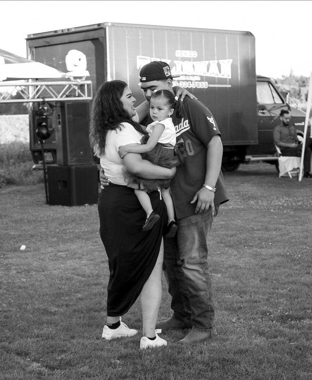 Couple sharing a kiss while holding their baby at an outdoor event, black and white photo.