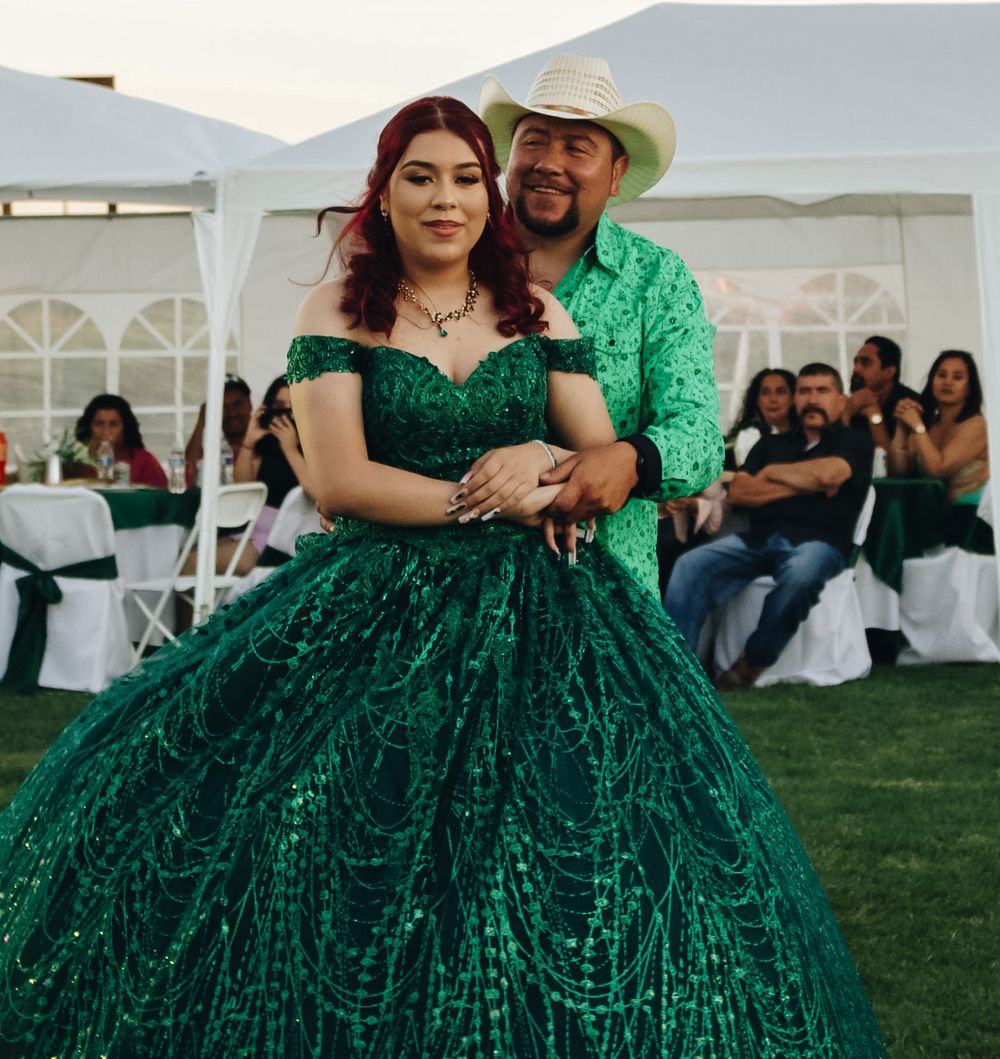 A young woman in a sparkling emerald green quinceañera gown poses with a man in a matching green shirt.