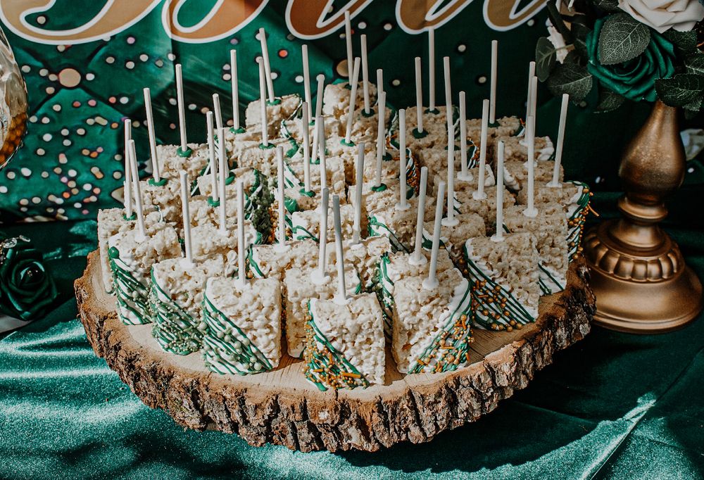 Elegant rice crispy treat pops with green drizzle displayed on a rustic wood slice at a quinceañera.