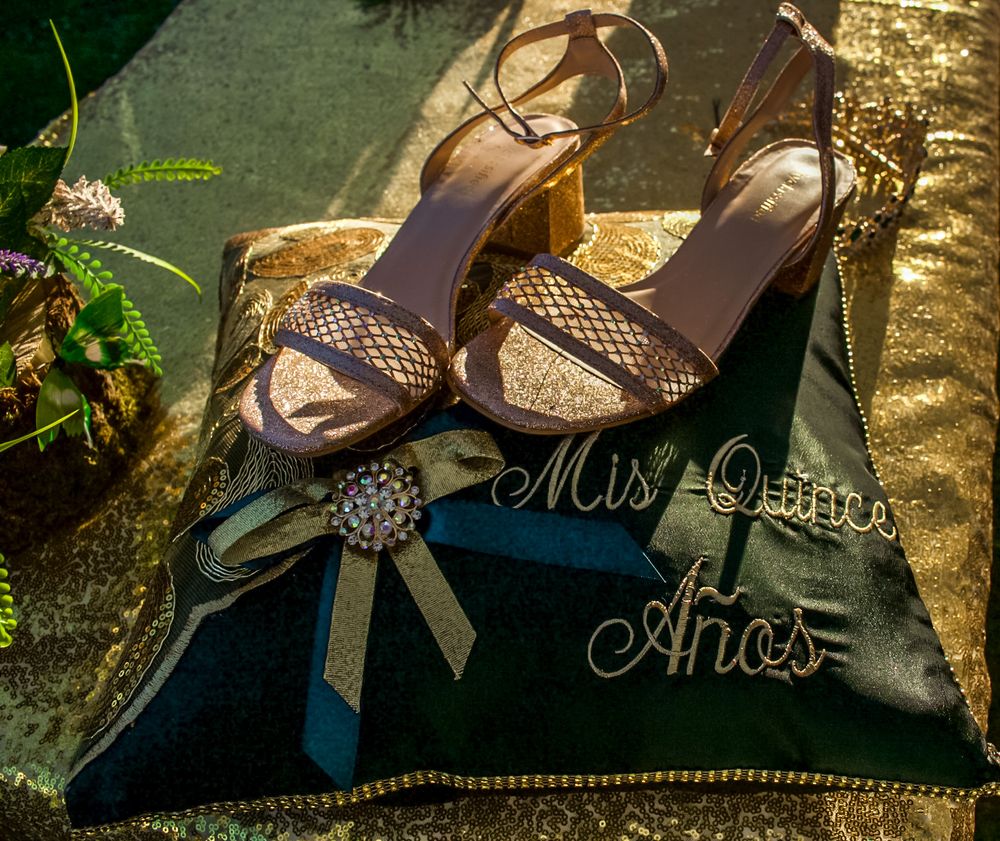 Gold heeled sandals rest on a green velvet quinceañera pillow embroidered with Mis Quince Anos.