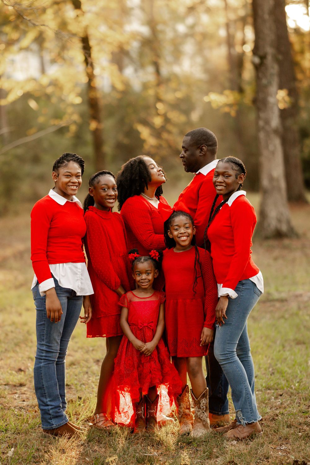 Family wearing coordinated red and white outfits poses together for a portrait in an autumn forest setting.