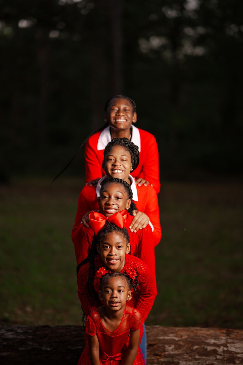 A group of five people wearing bright red outfits pose together in a creative stacked formation outdoors at dusk.