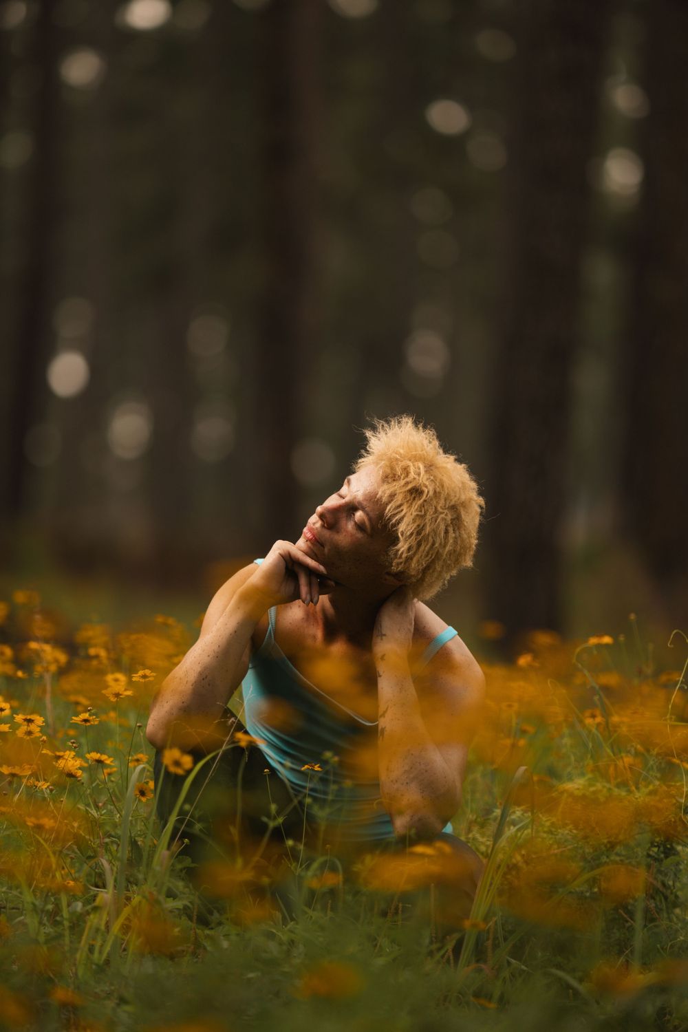 A person in a blue top sits among vibrant orange wildflowers in a dreamy forest setting at golden hour.