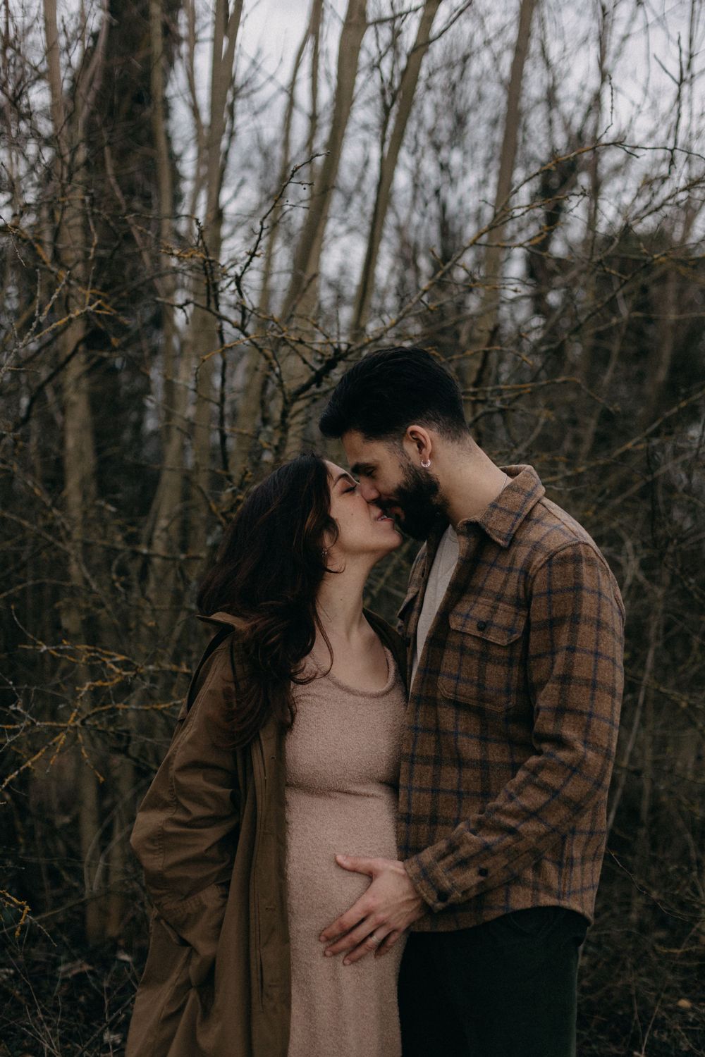 Tender embrace between couple in forest wearing plaid flannel and long dress.