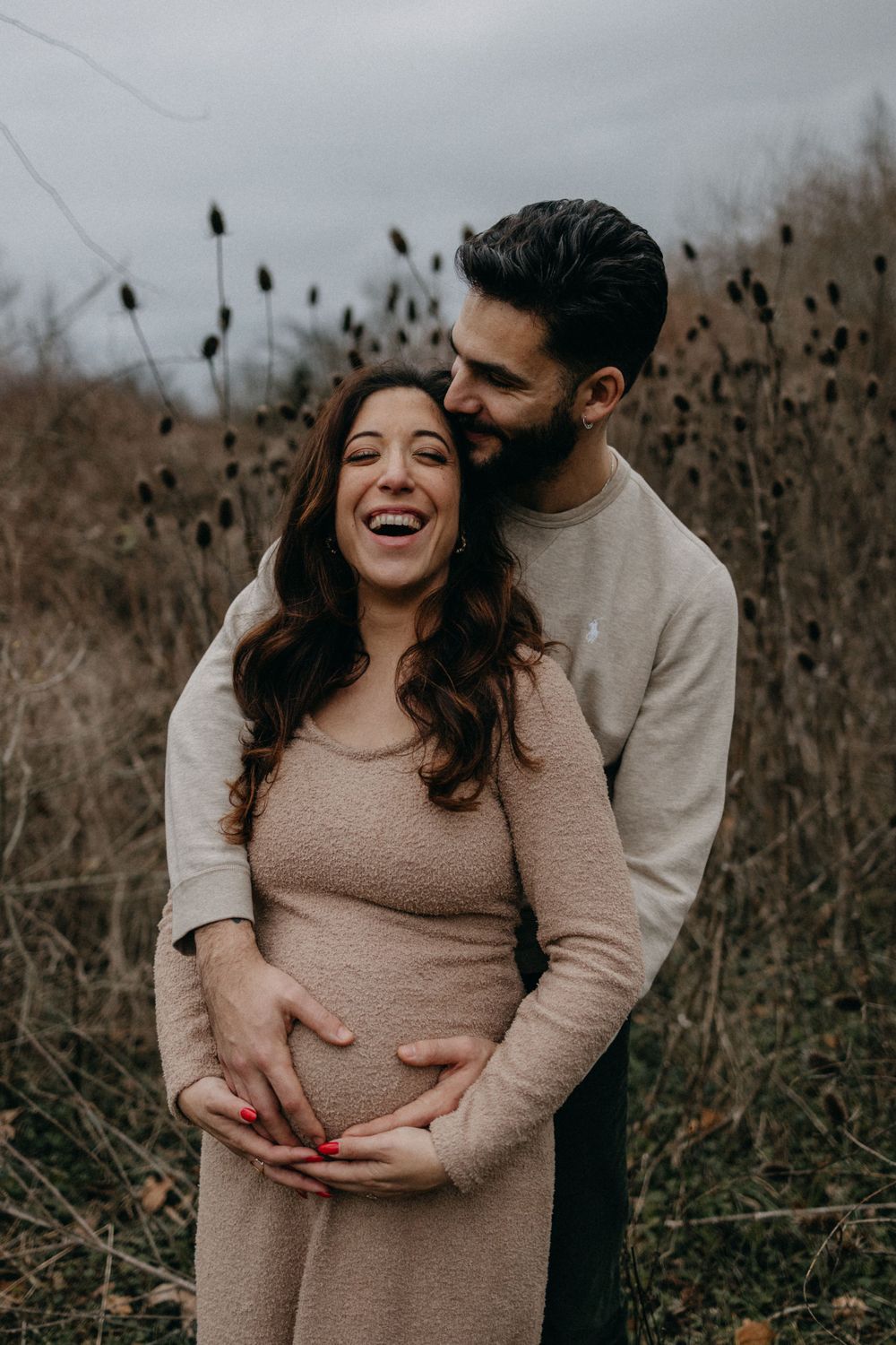 Expecting couple shares joyful moment in winter field.