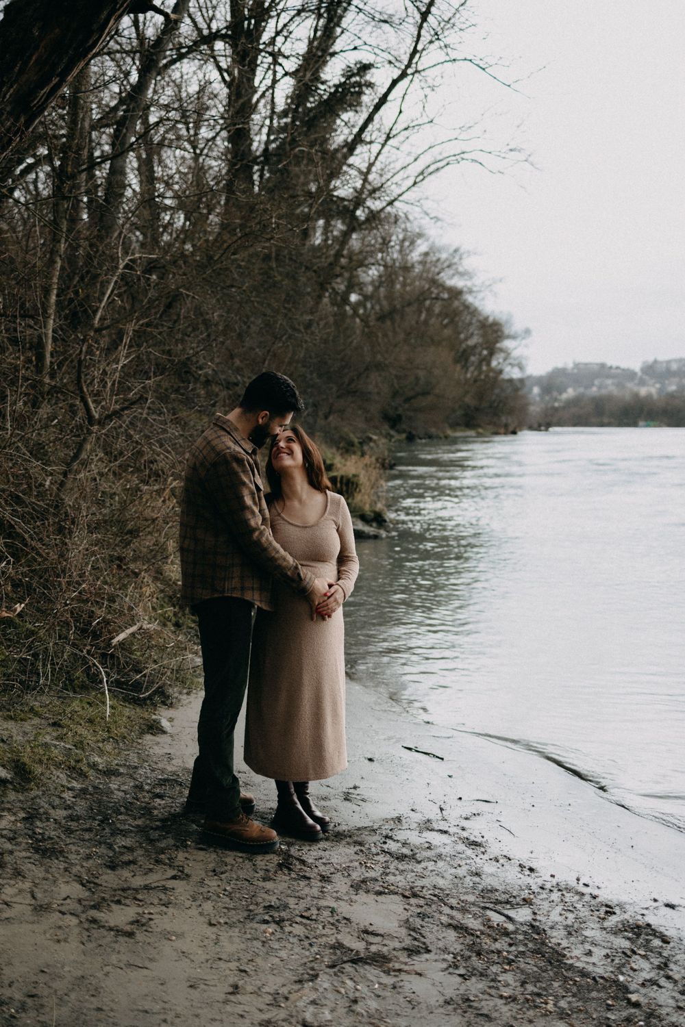 A couple stands intimately by a winter lakeshore during their maternity session.