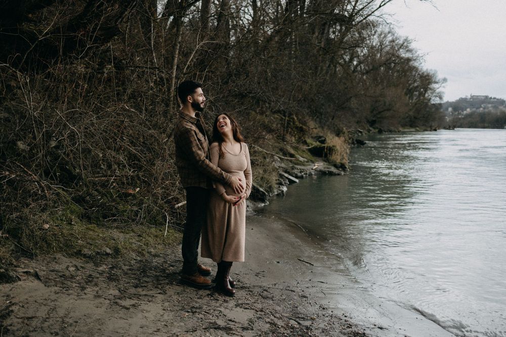 Expecting couple poses together on a rocky shoreline during their winter maternity shoot.